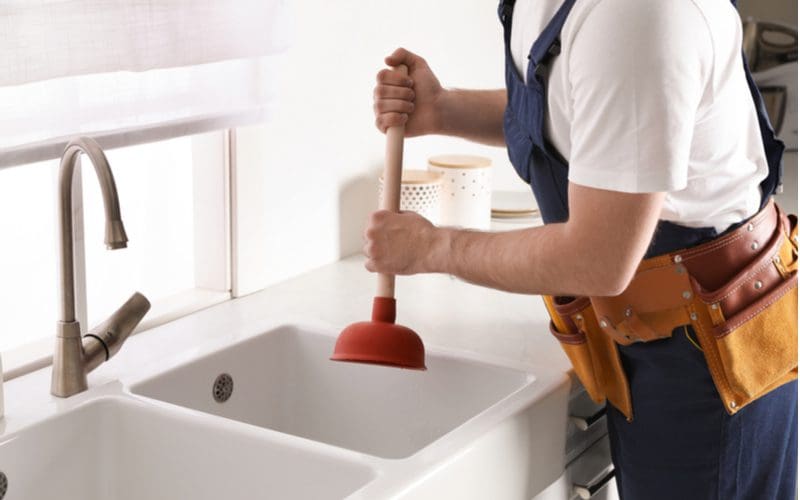Plumber using plunger to unclog kitchen drain