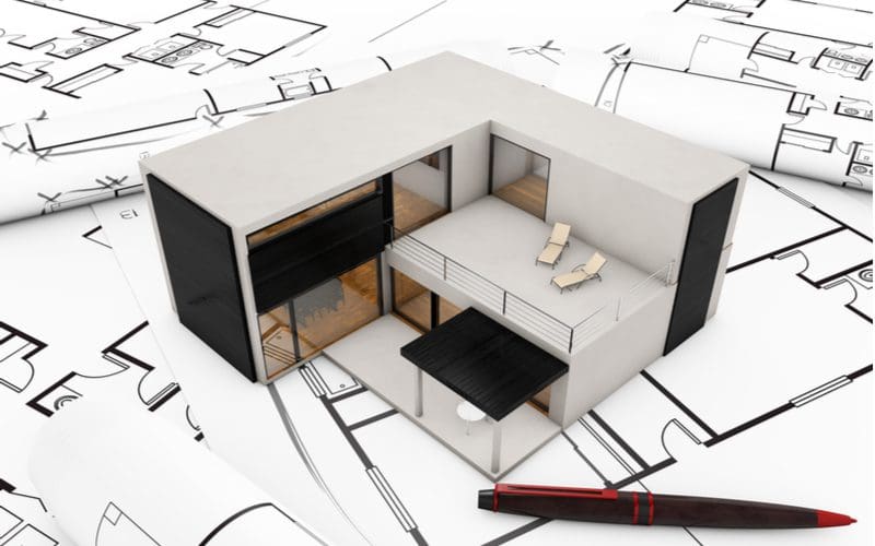 For a piece on modular home prices, a tiny model modular home sits on a black and white blueprint