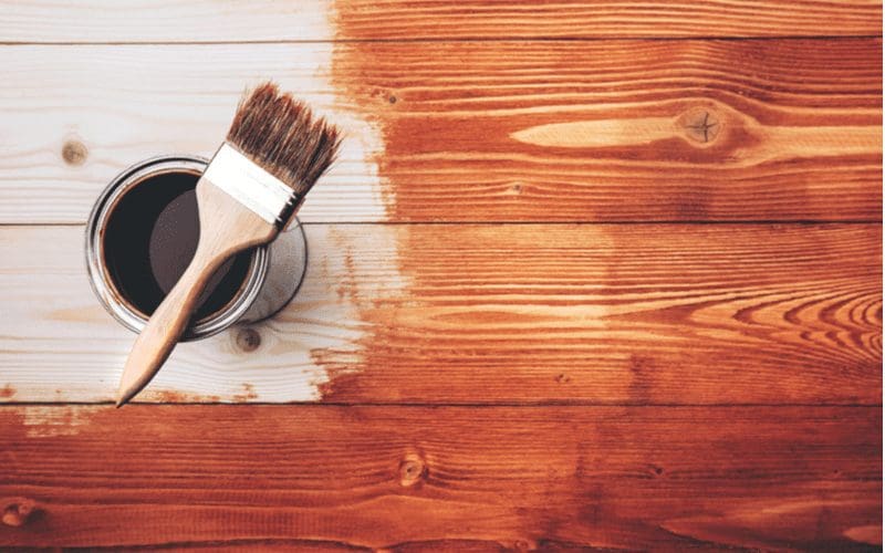 Paint brush sits on a deck while resting on a can of stain for a walkthrough on how to paint stained wood