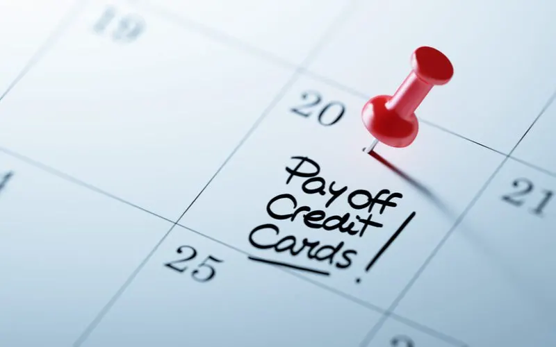Image of a calendar with a red pin in it holding up a note that says pay off credit cards