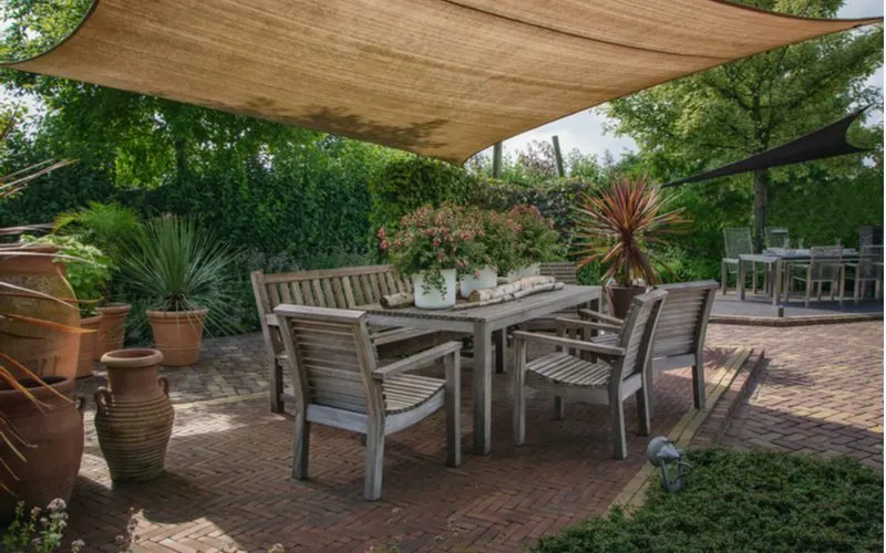 Big linen or burlap canvas shade for a patio stretched above a paver patio above a wooden table