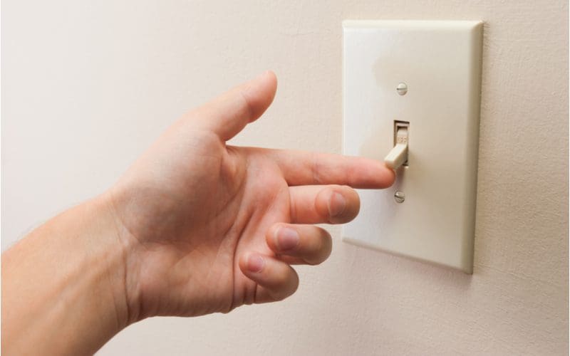Hand flipping a light switch up against an off-white eggshell wall