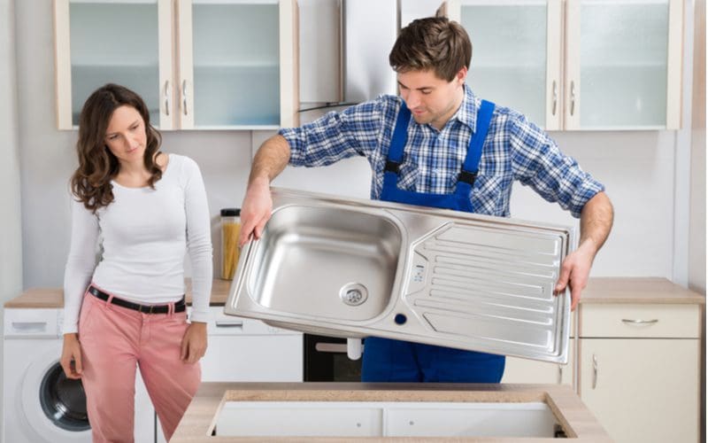 Woman observing a man installing a standard size kitchen sink in her home