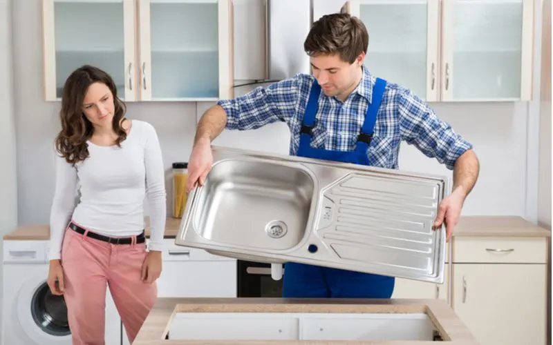 Woman observing a man installing a standard size kitchen sink in her home
