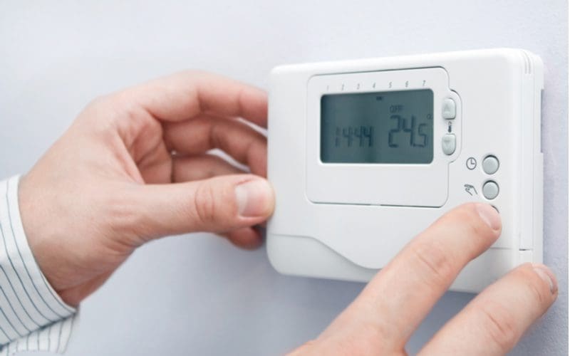 Two hands adjusting the temperature of a white electric thermostat