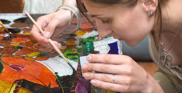 As an image for a piece on can you paint glass, a woman hunched over a piece of glass painting it