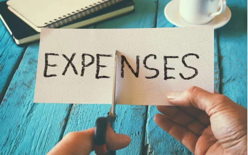 Woman holding a piece of cardboard that says Expenses in all capital letters and cutting it down the middle for a piece on how to save for a house