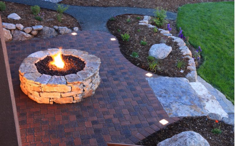 Paver patio idea with dark pavers mixed with light natural stone firepit and accents