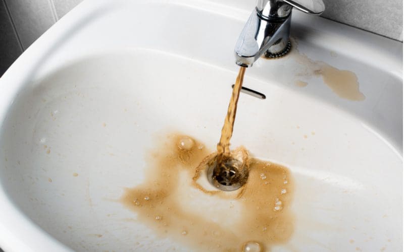 Dirty brown water running from a chrome faucet into a white sink