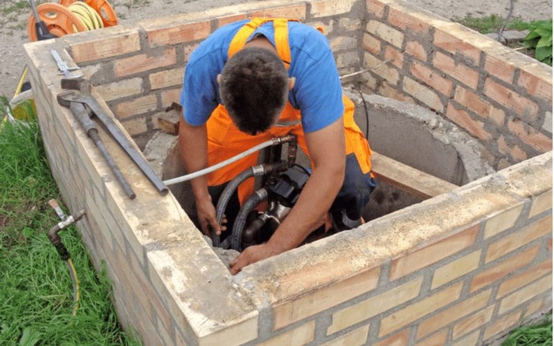 Well pump repair man fixing a pump inside a brick structure above a well