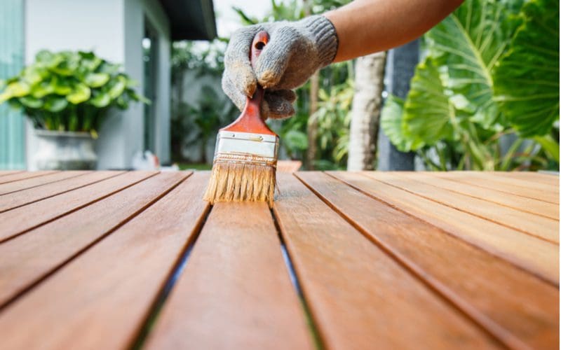 To help answer can you stain pressure treated wood, a person pulls a stain brush down a board