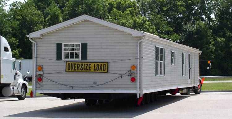 To illustrate how much it costs to move a mobile home, such a home sits on a trailer at a rest stop next to trees