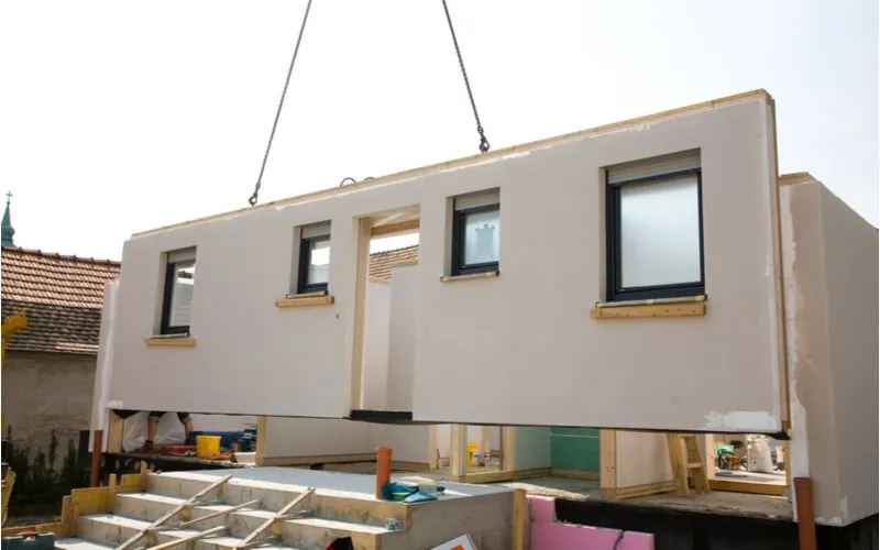 Crane putting a wall of a modular home onto the front of a house