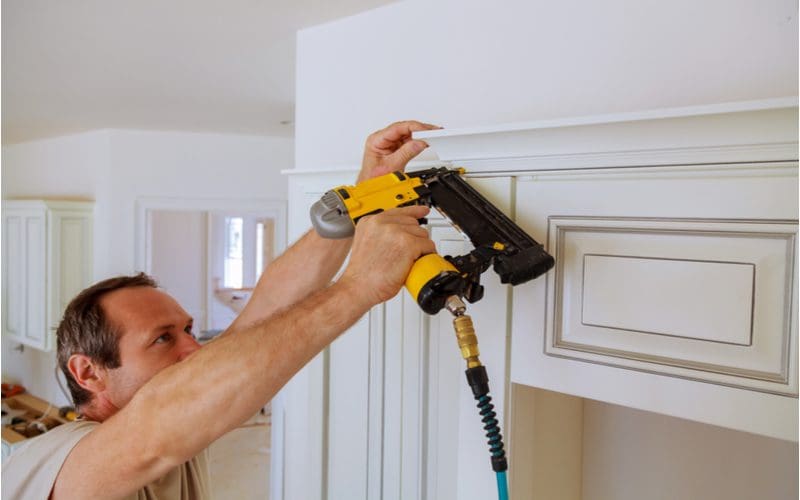 Guy using a brad nailer to nail a style of crown molding to a kitchen cabinet