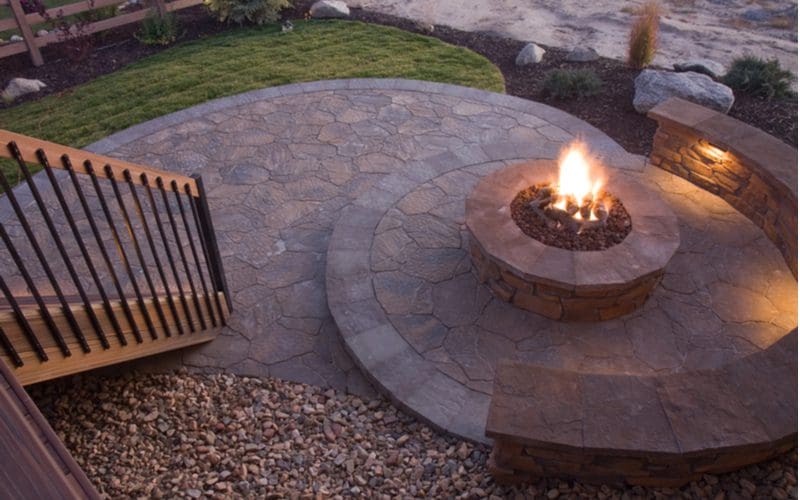 Beautiful paver patio firepit with multi levels with wooden stairs next to a sandy beach