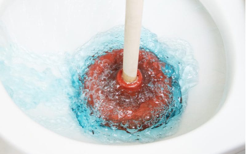Toilet bubbling while being plunged by a red and white plunger