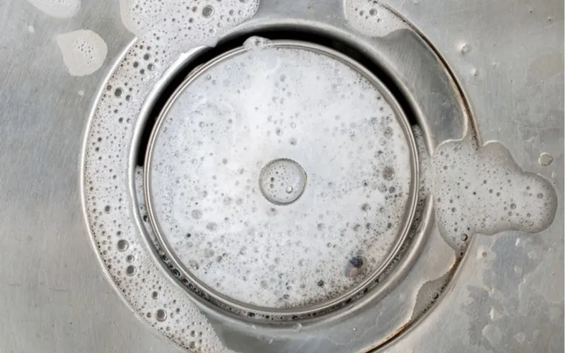 Image of a drain from which dish soap bubbles up in a stainless steel sink
