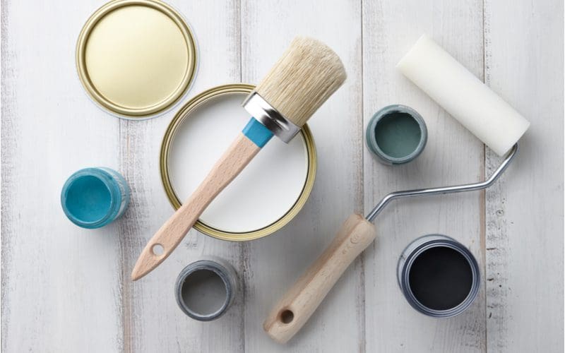 Image of painting supplies including a roller, paint cans, and a paint brush to answer Can You Paint Laminate Cabinets