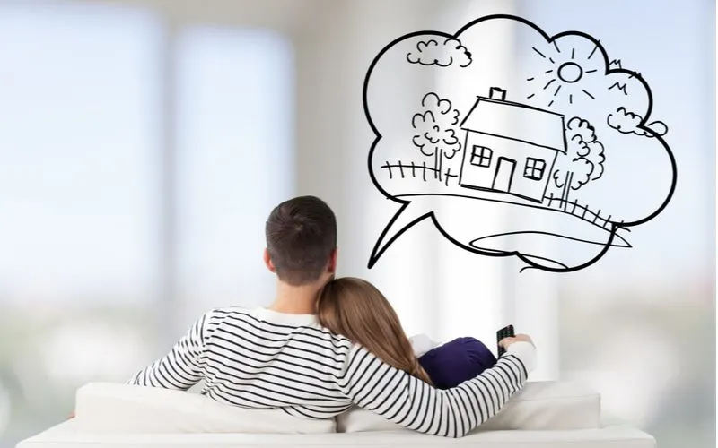 Couple dreaming about the best time to buy a home while a thought bubble pops above their head while sitting on a couch