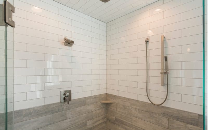Two-toned tile shower idea with white subway tiled running horizontally on top and bigger grey wood-look subway tiles on the bottom