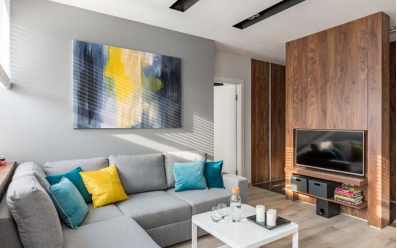 Vibrant yellow and blue wall art ties into the grey couch in the living room with natural wood paneling on the entertainment system