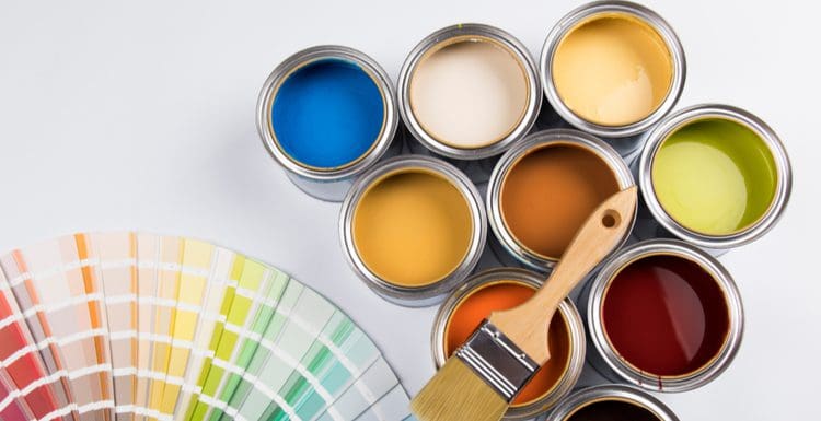 Various types of paint in all colors and finishes sit on a white background next to a brush and color wheel