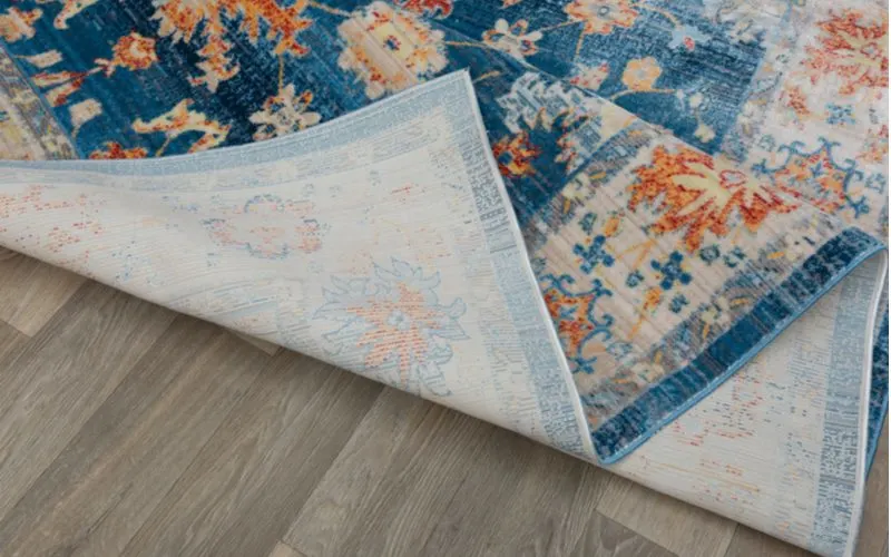 Blue and floral print rug bunched up on a grey wood floor