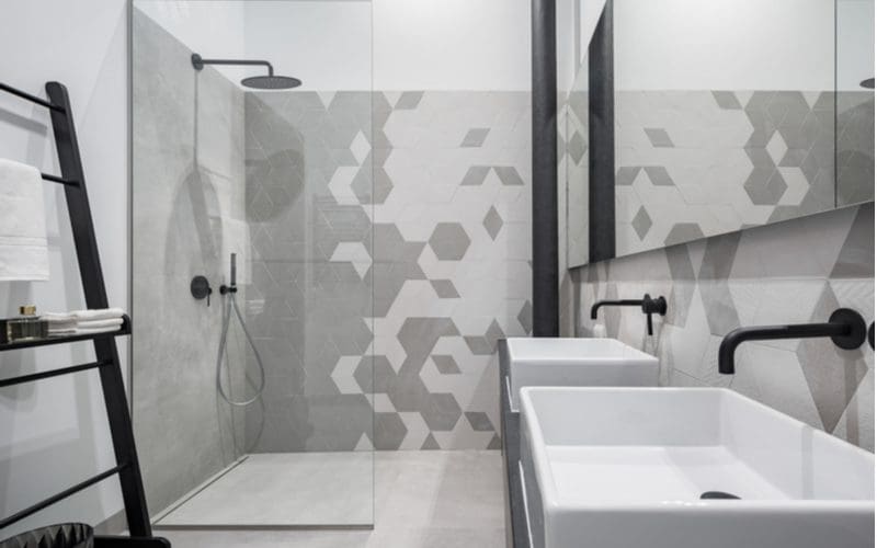 Hex gray tile bathroom idea with a tile shower surround with a walk-in shower without a door and a dark towel rack with a dark faucet protruding from the wall