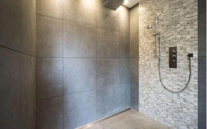 Simple walk in tile shower idea with big grey tiles on three walls and small grey and white horizontal subway tile accents on the wall with the fixtures