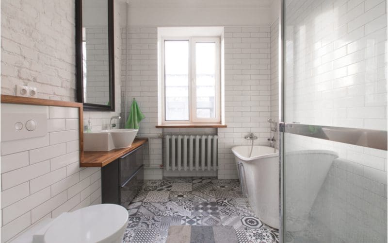 Simple grey tile bathroom idea featuring mosaic Spanish tile and a standalone white tub with a natural wooden shelf on which sits a sink bowl