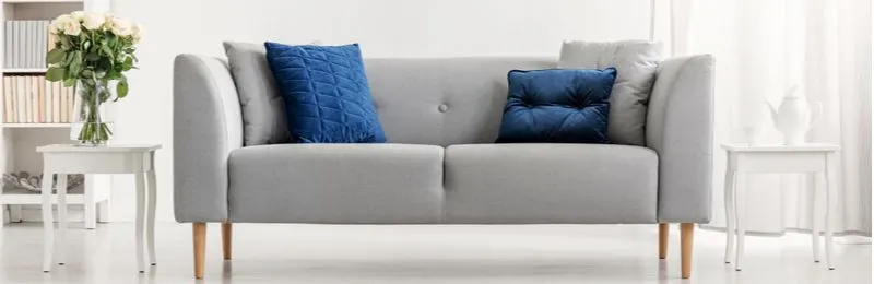 Grey couch living room ideas with contrasting end tables in white color with blue pillows as the statement piece
