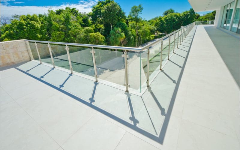 For a piece on front porch designs, a big concrete porch with glass railings overlooking a tree-lined concrete driveway