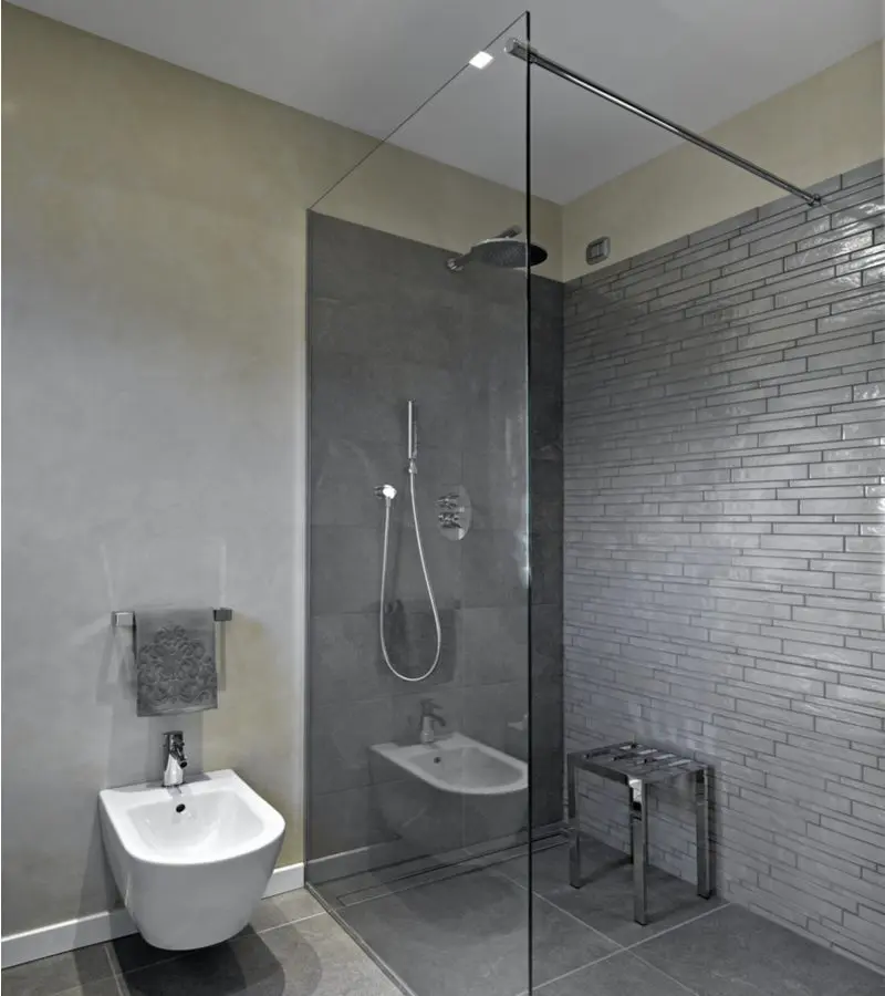 Rustic grey rectangle tile shower idea with two glass walls next to a white floating euro toilet