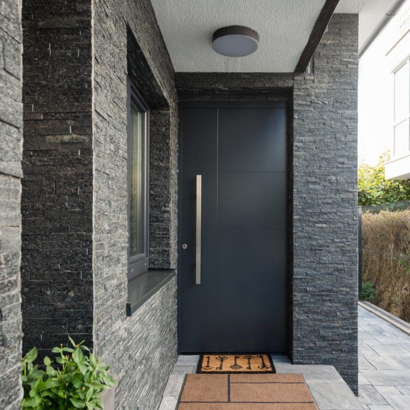 A simple yet elegant house entrance idea with a rock sided house with a big black metal door