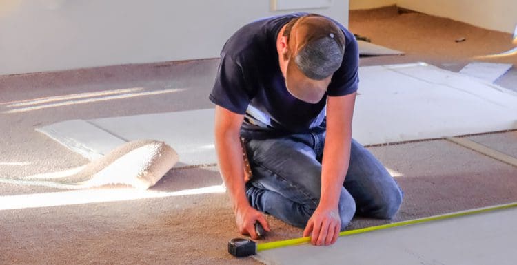 For a piece on how to install carpet, a guy using a tape measure to measure a piece of flooring while loose carpet sit around him