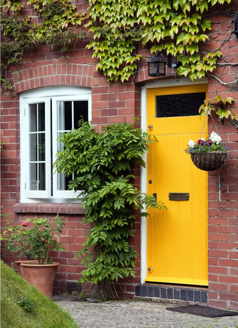 For a piece on the best front door colors for red brick house, a yellow painted door next to white windows on a red brick home