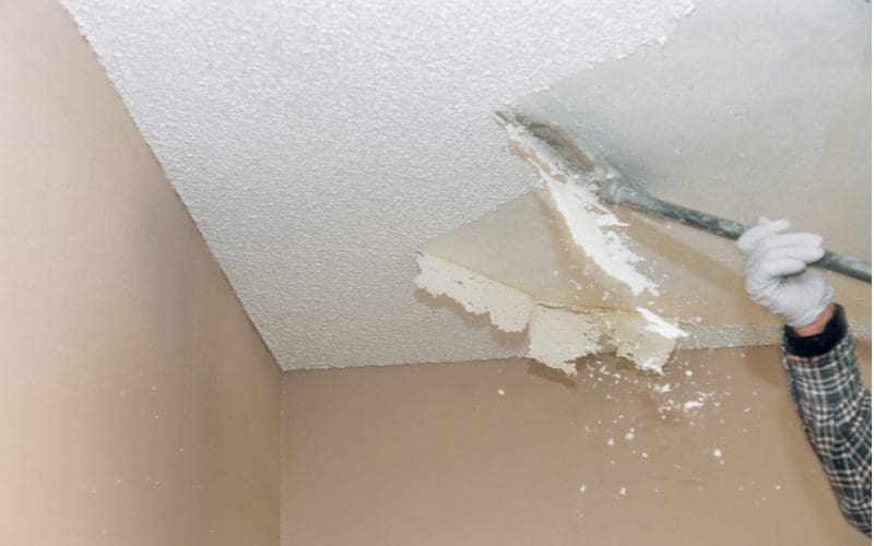 Worker removing a textured ceiling with a putty knife