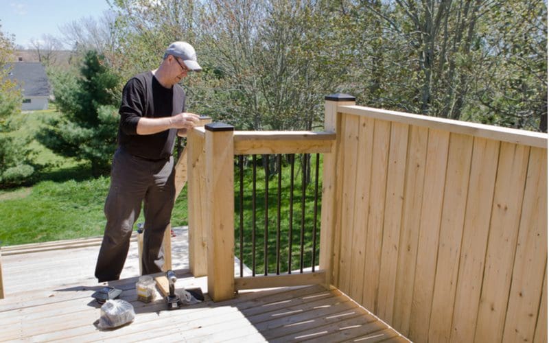 For a piece on deck railing ideas, a guy building a thick deck railing by some steps that lead to a small wooded backyard
