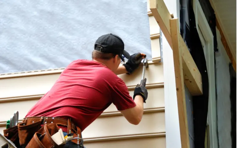 Man hammering in a piece of vinyl siding, one of the most popular types, into the exterior of a home