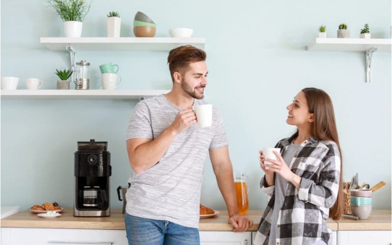 For a piece on coffee station ideas, a young couple standing together drinking cups of coffee in front of their coffee maker