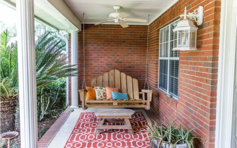 Front porch design with an overhang from which hangs a wooden porch swing next to a brick wall