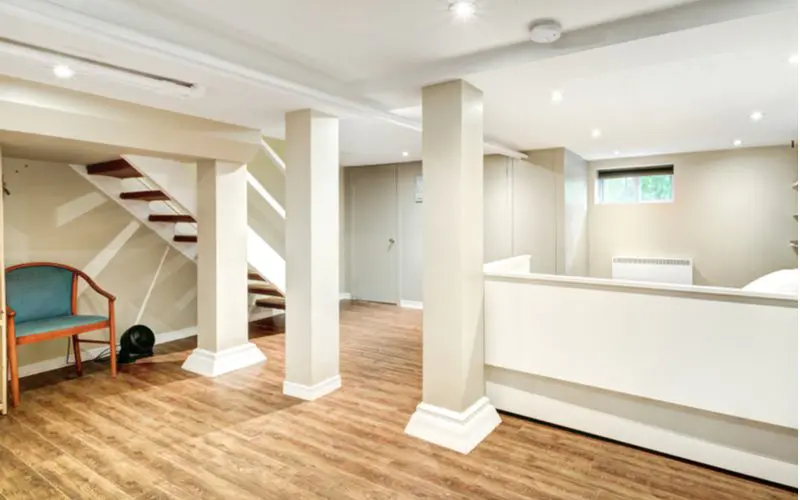 For a piece on basement ideas, a boxed-in half wall in a basement with light wooden floors and open steps with an open staircase