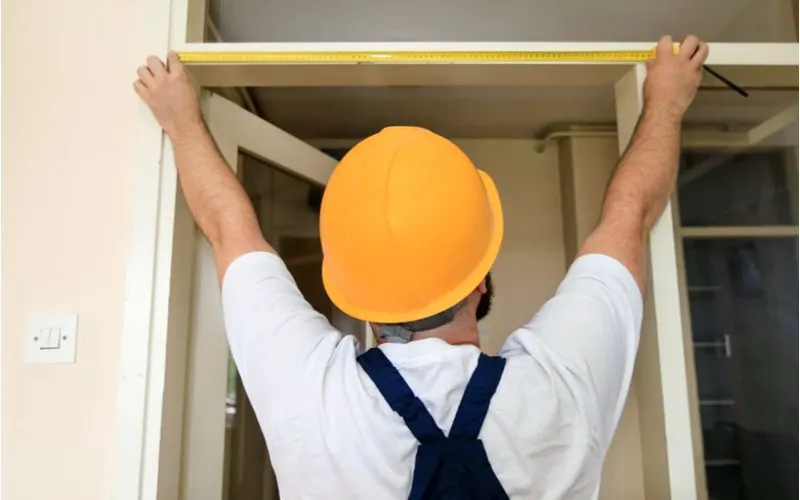 Image of a construction worker in a yellow hard hat taking the measurement of a French door size