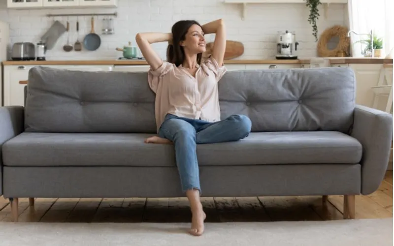 Gal in a open room next to a kitchen countertop relaxing on a standard dimension sofa