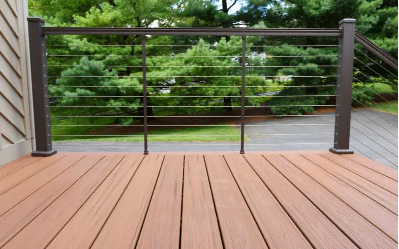 Thin metal cable deck railing idea running perpendicular to the straight composite deck boards 
