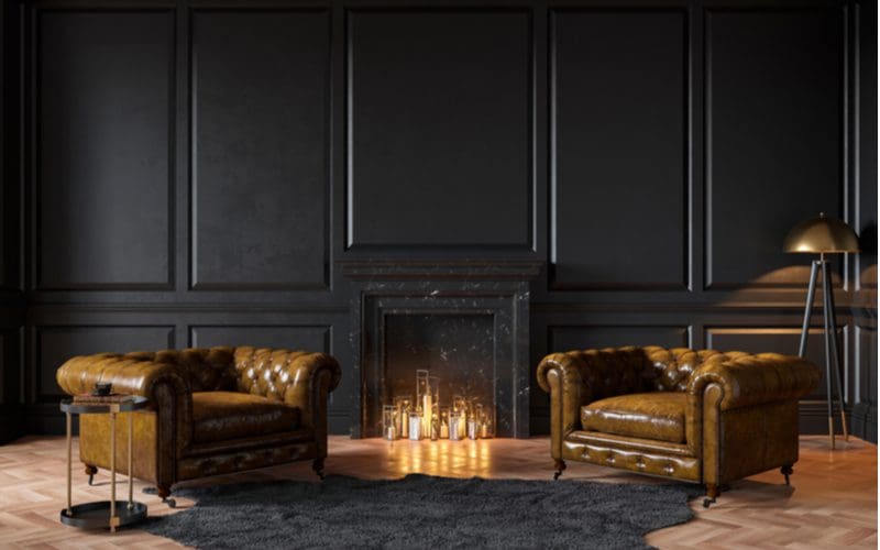 Black painted paneling around a living room with fireplace in the middle next to big leather chairs