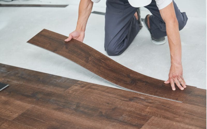 Man using vinyl planks as a form of basement flooring and laying it down while kneeling