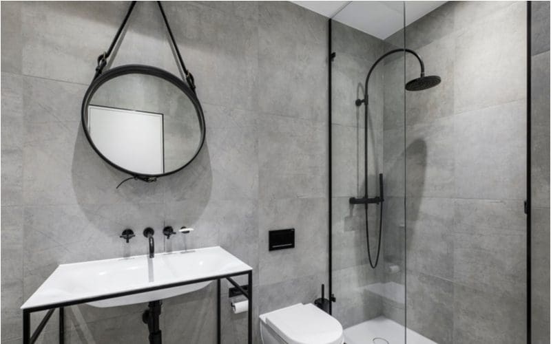 Grey tile bathroom idea with a round mirror and a simple glass walk-in shower with a half glass door and oil rubbed bronze fixtures