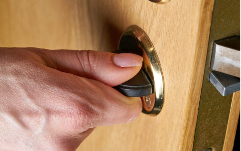 Article describing the part of a door knob, with a close-up of a hand turning a door deadbolt lock