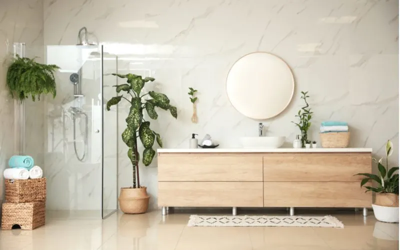 Image for a piece on bathroom inspiration featuring lots of green plants scattered about an otherwise open and drab marble-walled bathroom
